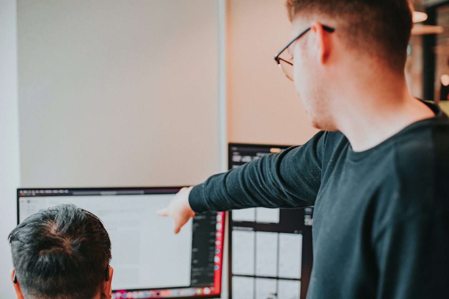 Man with glasses points at computer screen during office meeting.