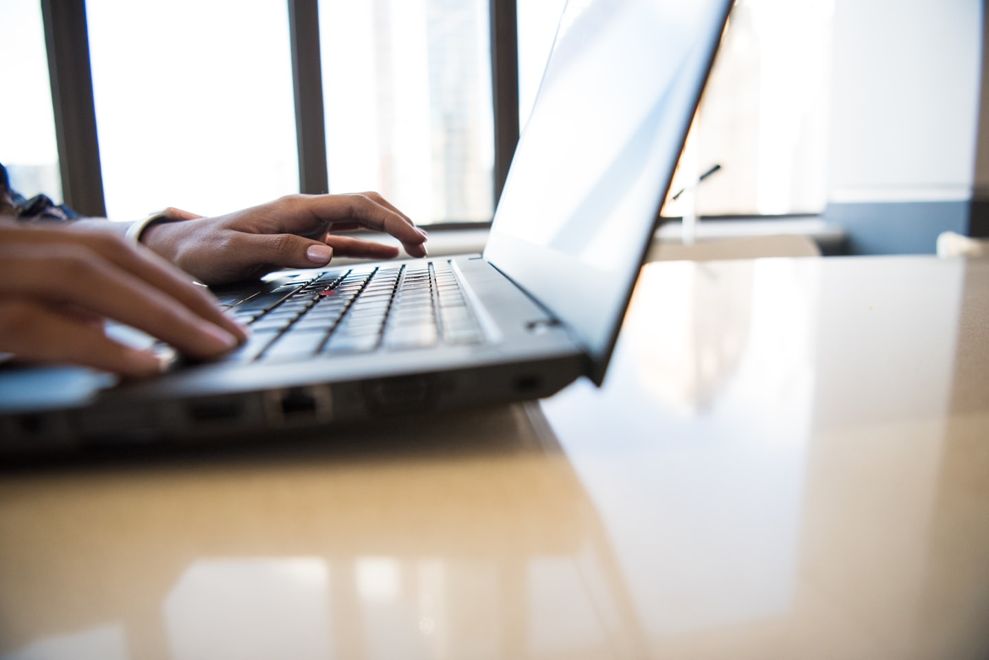 Dark-skinned hands typing on a laptop keyboard.